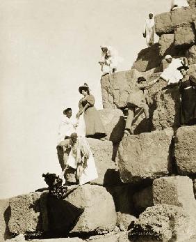 Tourists ascending the pyramids with native guides (b/w photo) 