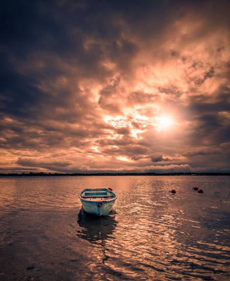 verlassenes Boot am See mit Sonnenschein und Wolken