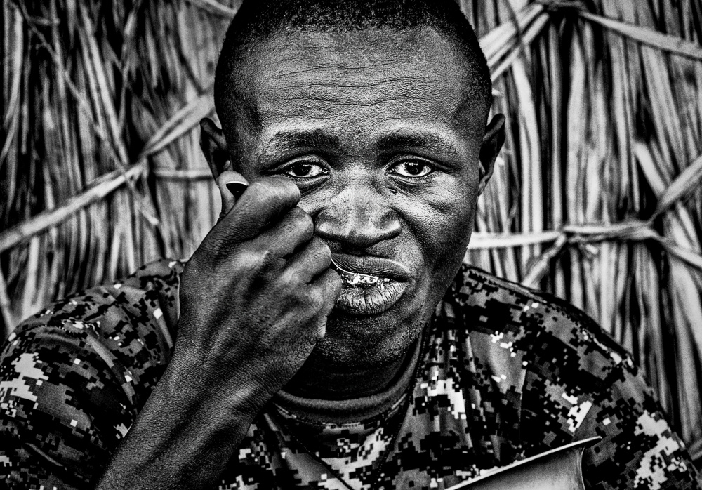 El Molo ethnic man eating at the entrance of his home. von Joxe Inazio Kuesta Garmendia
